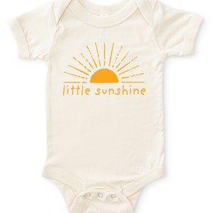 Natural white short sleeve infant bodysuit with mustard yellow little sunshine text with boho sun rays design printed on front, laying flat on white background