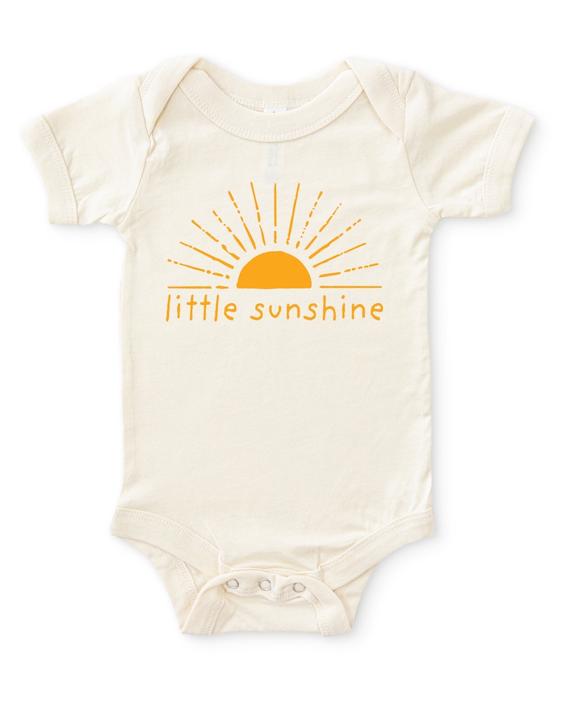 Natural white short sleeve infant bodysuit with mustard yellow little sunshine text with boho sun rays design printed on front, laying flat on white background