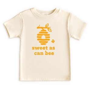Natural white short sleeve toddler crew neck tee with mustard yellow sweet as can bee text with flying bumble bee outisde beehive hanging off branch print, laying flat on white background