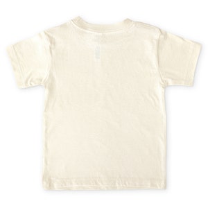 Back view of natural cream colored short sleeve toddler crew neck tee laying flat on white background