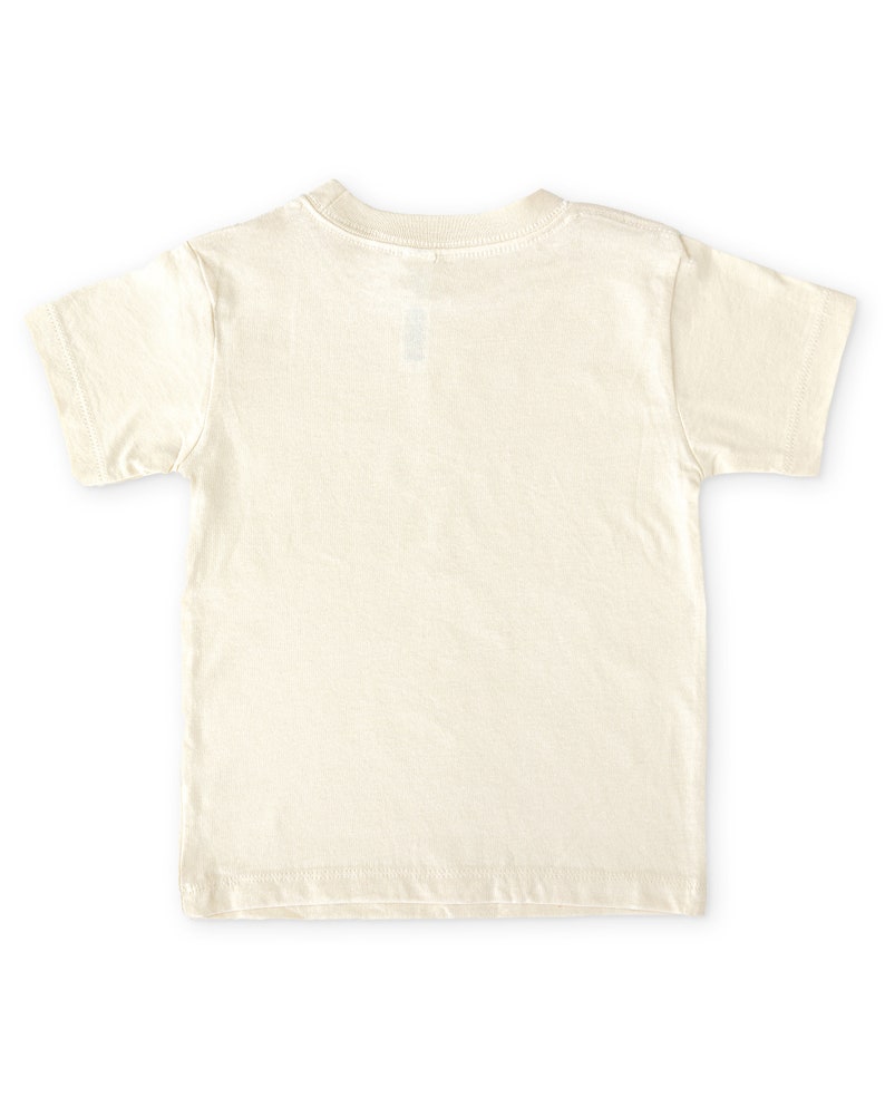 Back view of natural cream colored short sleeve toddler crew neck tee laying flat on white background