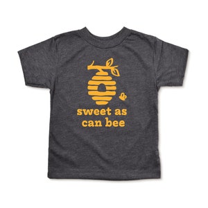 Heather dark grey short sleeve toddler crew neck tee with mustard yellow sweet as can bee text with flying bumble bee outisde beehive hanging off branch print, laying flat on white background