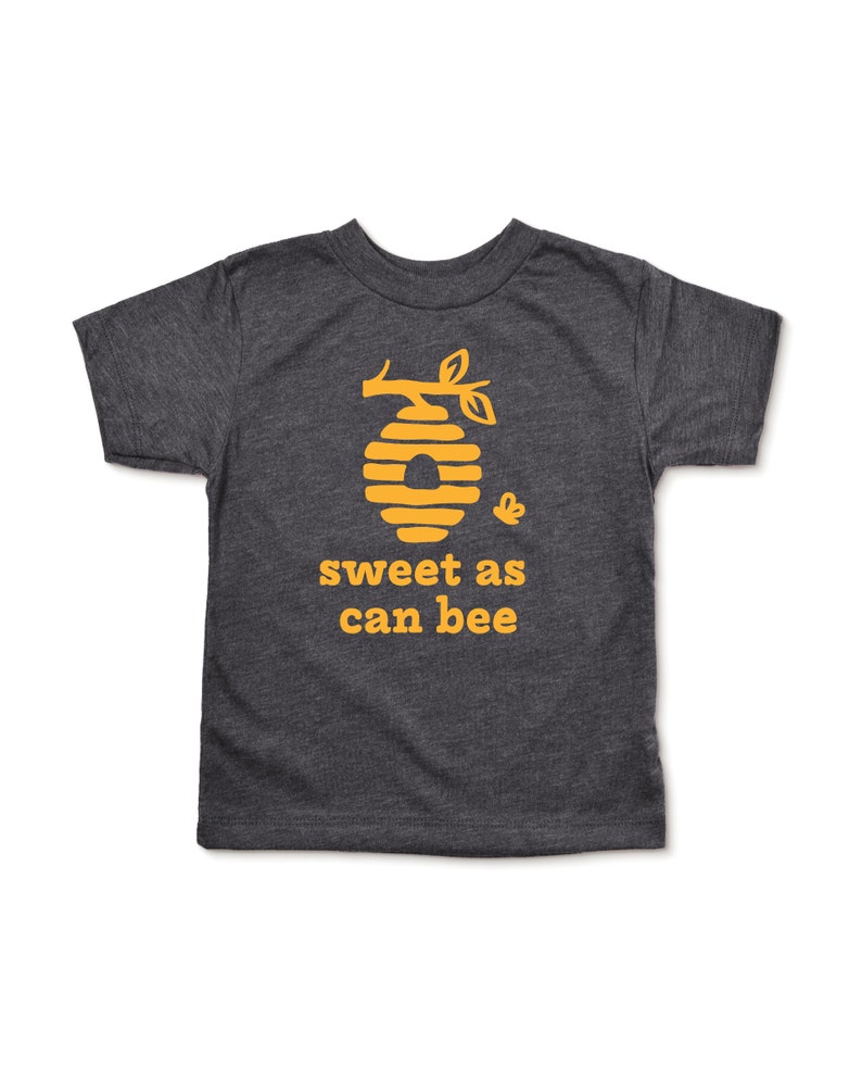 Heather dark grey short sleeve toddler crew neck tee with mustard yellow sweet as can bee text with flying bumble bee outisde beehive hanging off branch print, laying flat on white background