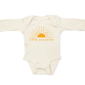 K&ouml;nnte beinhalten: Ein wei&szlig;er lang&auml;rmeliger Baby-Strampler mit einem orangefarbenen Sonnenmotiv und dem Text "little sunshine".