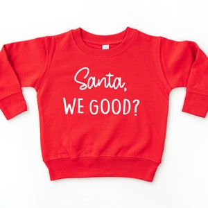 Red long sleeve crew neck toddler sweatshirt with white Santa, WE GOOD? graphic print, laying flat on white background