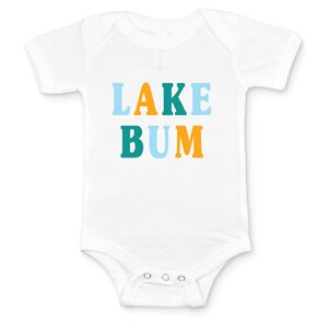 White short sleeve baby bodysuit with alternating light blue, mustard yellow and teal blue LAKE BUM text print on front, laying flat on white background