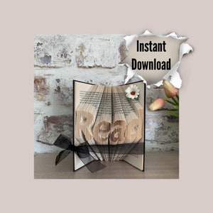 May include: A book art sculpture of the word "Peace" folded from the pages of a book. The sculpture is displayed on a wooden surface with a black ribbon and a white flower.