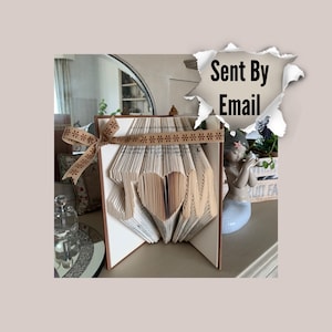 May include: A book art sculpture of the word "MOM" with a heart in the middle. The sculpture is made from the pages of a book and is decorated with a brown ribbon with a floral pattern.