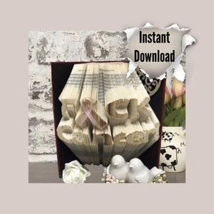 May include: A book art sculpture with the words "F**K CANCER" formed from folded pages. The sculpture is displayed on a red shelf with a pink ribbon on the letter "C".