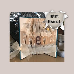 May include: A book art sculpture of the word "Friends" made from the pages of a book. The sculpture is standing on a table with a teal bookend and a white ribbon.
