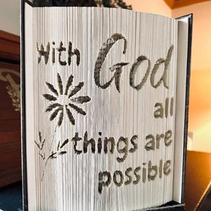 May include: A book with the words "With God all things are possible" cut out of the pages. The words are surrounded by a decorative flower design.