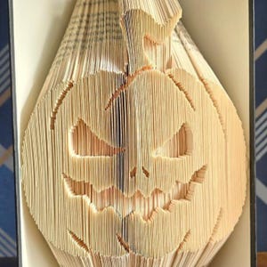 May include: A unique Halloween decoration crafted from the pages of a book. The pages are folded and cut to create a jack-o'-lantern face. The pumpkin has a stem and a carved face with triangular eyes and a jagged mouth.