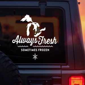 May include: A white decal on the back of a dark gray car. The decal features a silhouette of the state of Michigan, the words "Always Fresh", a wavy line, and the text "Sometimes Frozen". A snowflake icon is below the text.