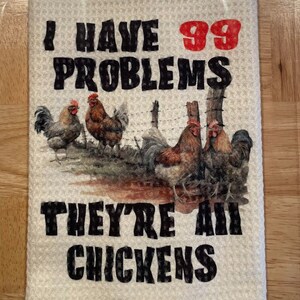 May include: A kitchen towel with a humorous saying: "I have 99 problems, they're all chickens." The towel features a graphic of four chickens in a farmyard setting.