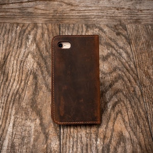 May include: A brown leather phone case with a stitched edge and a camera hole.