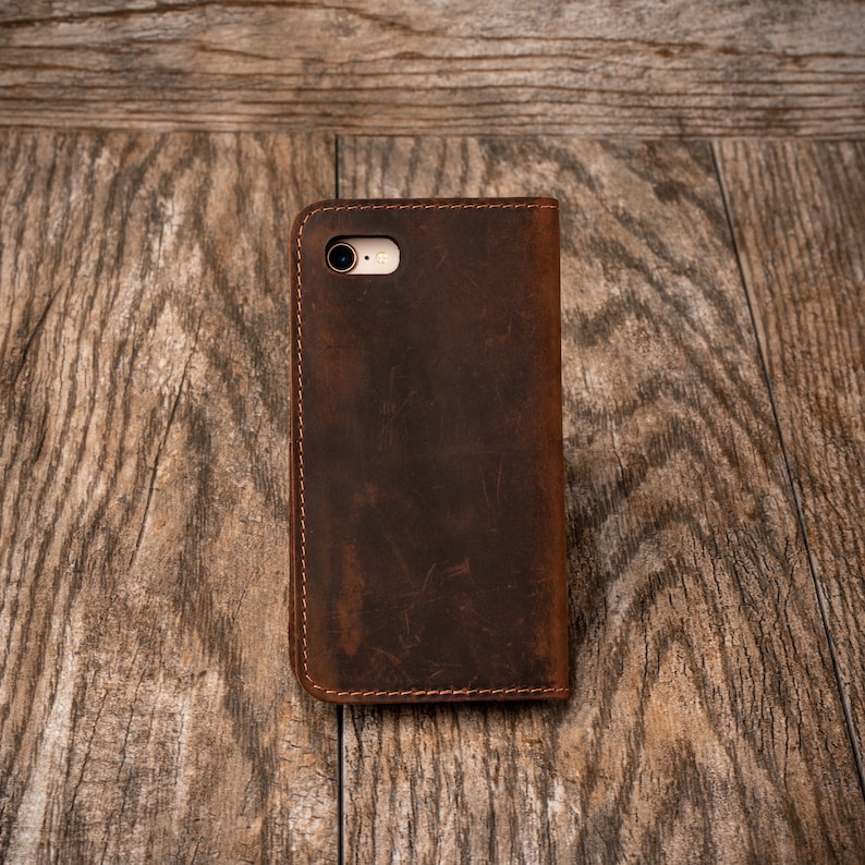 May include: A brown leather phone case with a stitched edge and a camera hole.