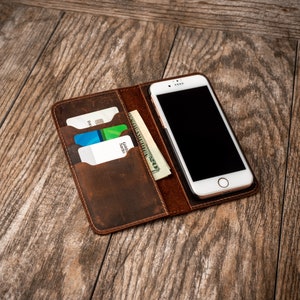 May include: A brown leather wallet with a phone case and slots for cards and cash. The phone case has a white phone with a black screen inside.