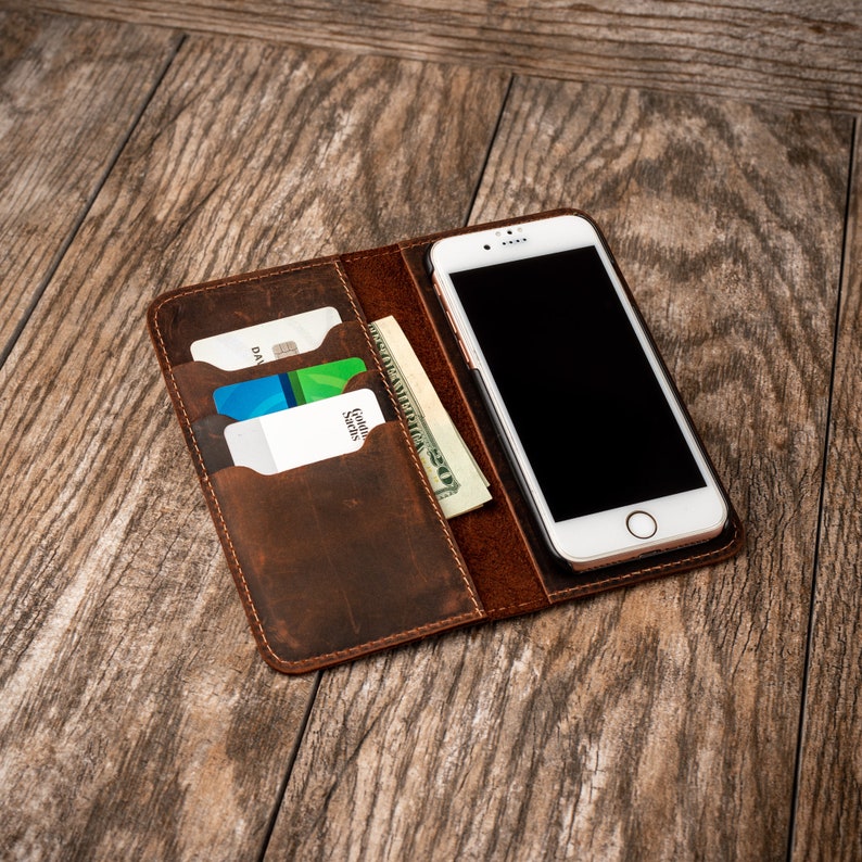 May include: A brown leather wallet with a phone case and slots for cards and cash. The phone case has a white phone with a black screen inside.