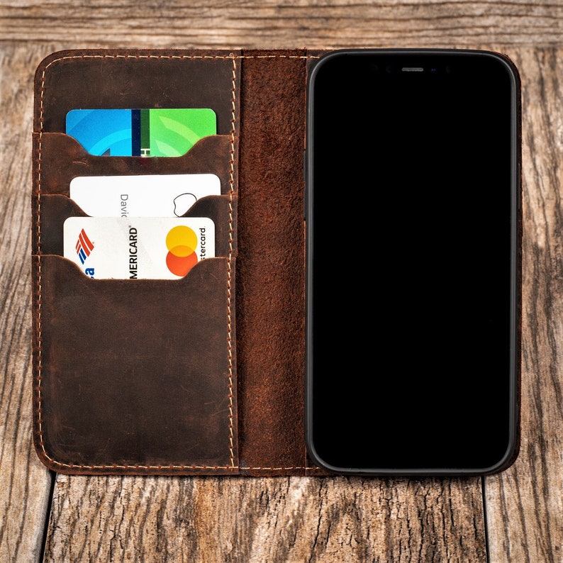 May include: A brown leather phone case with three card slots. The case has a stitched edge and a black phone screen.