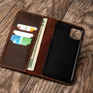 May include: A brown leather phone case with a built-in wallet. The case has slots for credit cards and a pocket for cash. The phone case is open and the phone is visible.