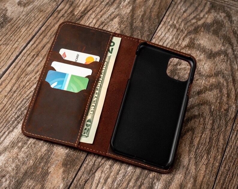 May include: A brown leather phone case with a built-in wallet. The case has slots for credit cards and a pocket for cash. The phone case is open and the phone is visible.