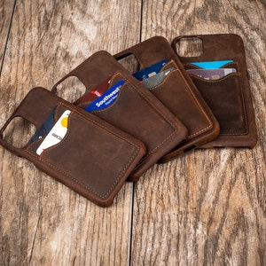 May include: Four brown leather phone cases with card slots. The cases are stacked on top of each other, with the top case showing a credit card in the slot.