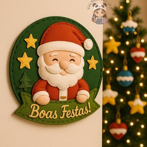 Pode incluir: Decoração de Natal em feltro com o Pai Natal com barba branca e fato vermelho, sobre um fundo verde com estrelas amarelas e uma árvore de Natal. A faixa diz "Boas Festas!"