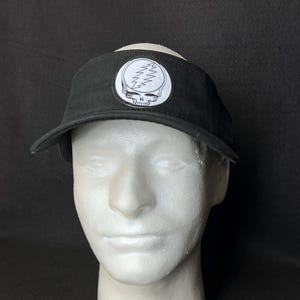 May include: Black visor with a white and black Steal Your Face logo patch. The visor has a curved brim and a fabric band. The logo features a skull with a lightning bolt design.