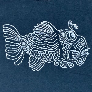 Könnte beinhalten: Dunkelmarineblaues T-Shirt mit einem weißen, stilisierten Fischdesign. Der Fisch ist mit Linien und Mustern detailliert, was ihm ein einzigartiges, künstlerisches Aussehen verleiht. Das Design ist auf dem Shirt zentriert.