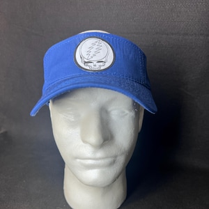 May include: A blue visor with a white and black Steal Your Face logo. The visor is made of a durable fabric and features a curved brim. The logo is a stylized skull with a lightning bolt.