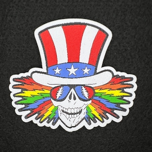 May include: A white embroidered patch featuring a skull wearing sunglasses and an Uncle Sam hat with red, white and blue stripes and stars. Rainbow lightning bolts emerge from the top of the skull's head.