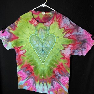 May include: A tie-dye t-shirt featuring a green, blue and white heart design. The shirt is a light green colour with shades of pink, red and blue.