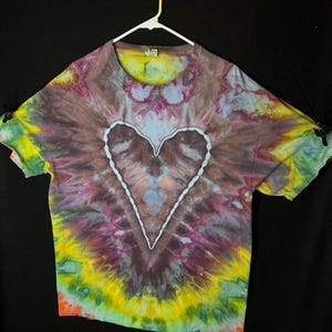 May include: A tie-dye t-shirt with a large heart design in the centre. The shirt is a mix of purple, blue, green, yellow, and orange colours.