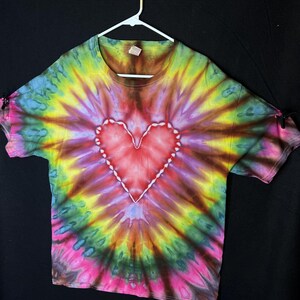 May include: A tie-dye t-shirt with a large, red heart in the centre. The shirt is a mix of yellow, green, purple, and pink.