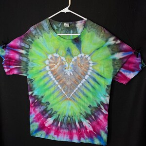 May include: A tie-dye t-shirt featuring a large heart design in shades of green, blue, pink, and brown. The heart is surrounded by a swirling pattern of colours.