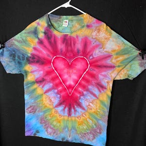 May include: A tie-dye t-shirt with a large white heart in the centre. The shirt is a mix of blue, green, yellow, and red colours.
