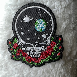 May include: Embroidered patch with a skull design, featuring a starry night sky. The skull is surrounded by red roses and green leaves. The patch is black, white, red, green, and blue.