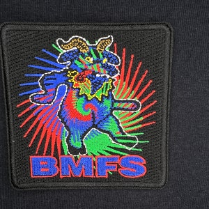 May include: A black patch featuring a colourful, tie-dye-style cartoon creature with horns and the text "BMFS" in blue.