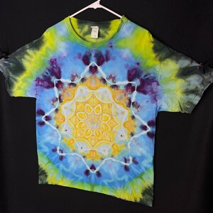 May include: A tie-dye t-shirt featuring a yellow, blue and purple mandala design. The shirt is on a hanger against a black background.