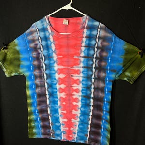May include: A tie-dye t-shirt with a red, blue and green colour scheme. The shirt has a vertical pattern with a V-shaped design in the centre.