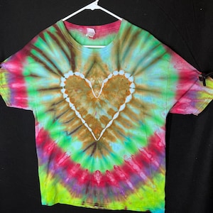 May include: A tie-dye t-shirt with a brown heart design in the centre. The shirt is a blend of green, blue, pink, and yellow colours.