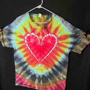 May include: A tie-dye t-shirt with a red heart design in the centre. The shirt is a blend of yellow, orange, red, blue, green, and black.