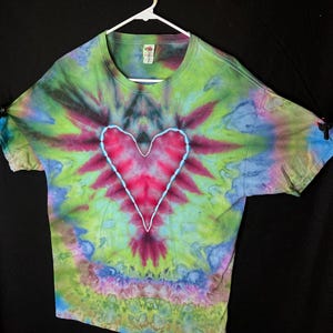 May include: A tie-dye t-shirt with a large, red heart design in the centre. The shirt is a blend of green, blue, and purple colours.