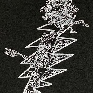 May include: Black graphic design featuring a skeleton with a floral headpiece, integrated into a white lightning bolt shape. The skeleton is posed with one arm raised. The design is detailed and intricate, with a focus on the contrast between the black background and white illustration.