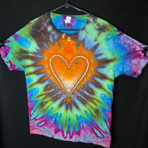May include: A tie-dye t-shirt with a white heart design in the centre. The shirt is a mix of blue, green, orange, pink, and purple colours.