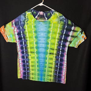 May include: A tie-dye t-shirt with a vibrant green, blue, and purple colour scheme. The shirt has a vertical pattern with a light blue centre.