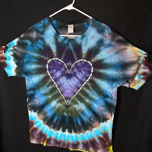 May include: A tie-dye t-shirt with a purple heart in the centre. The shirt is a dark blue, black, and yellow colour.