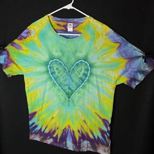 May include: A tie-dye t-shirt with a green heart design in the centre. The shirt is a blend of yellow, green, blue, and purple.