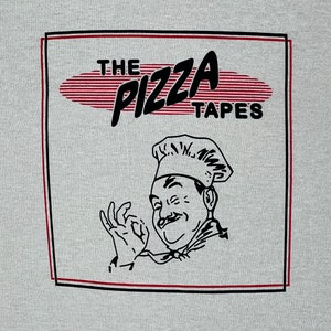 Könnte beinhalten: Eine Schwarzweißillustration eines Kochs mit einem rot-weiß gestreiften Oval hinter ihm, auf dem in schwarzer Schrift "THE PIZZA TAPES" steht.
