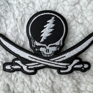 Peut inclure: Un patch brodé noir et blanc représentant un crâne avec un éclair à l'intérieur. Le crâne est croisé par deux épées.